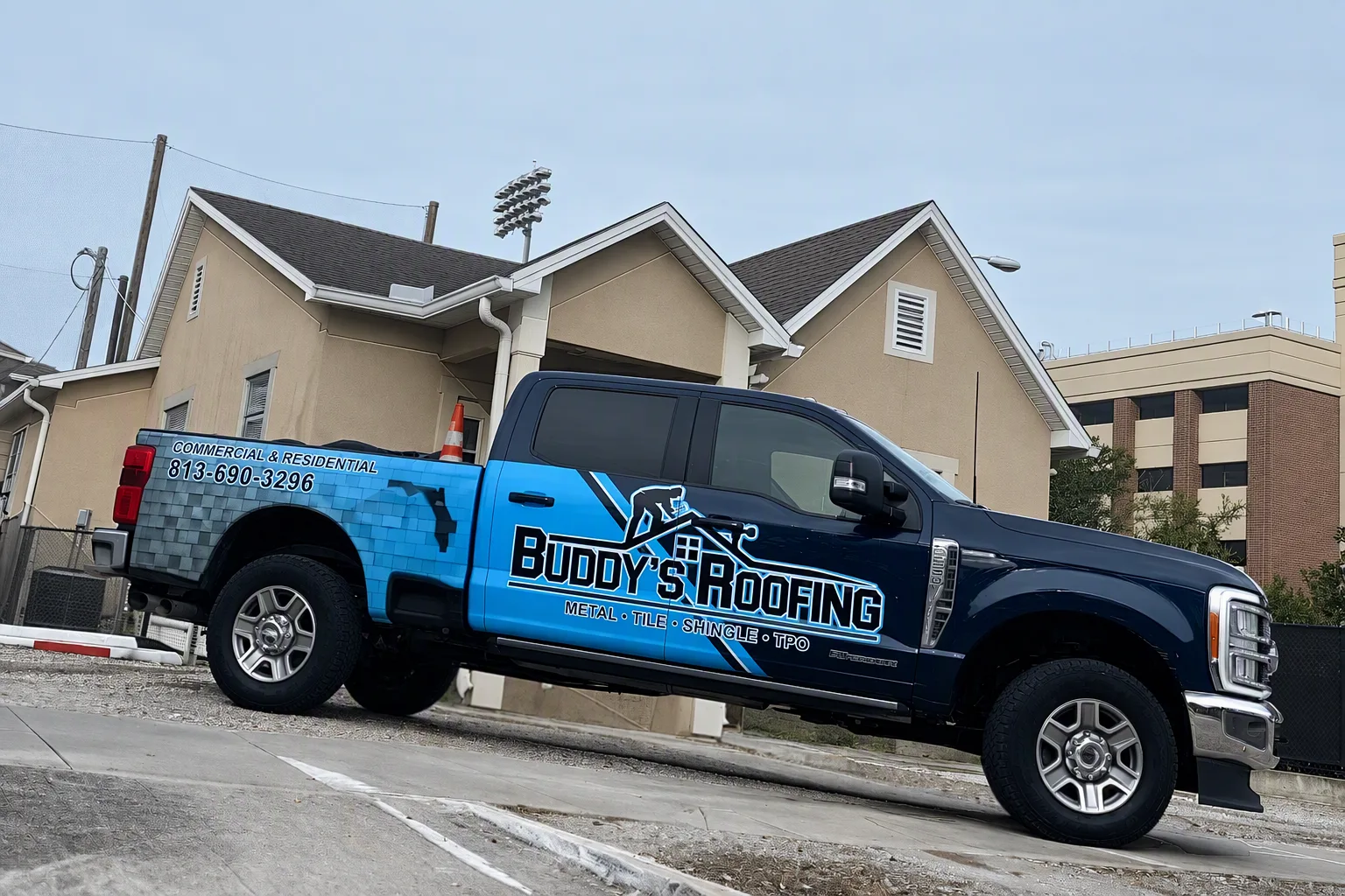 A small team of roofing technicians in plain navy work shirts standing together outside a well-kept suburban home, relaxed and not posed, one navy service van visible just behind them