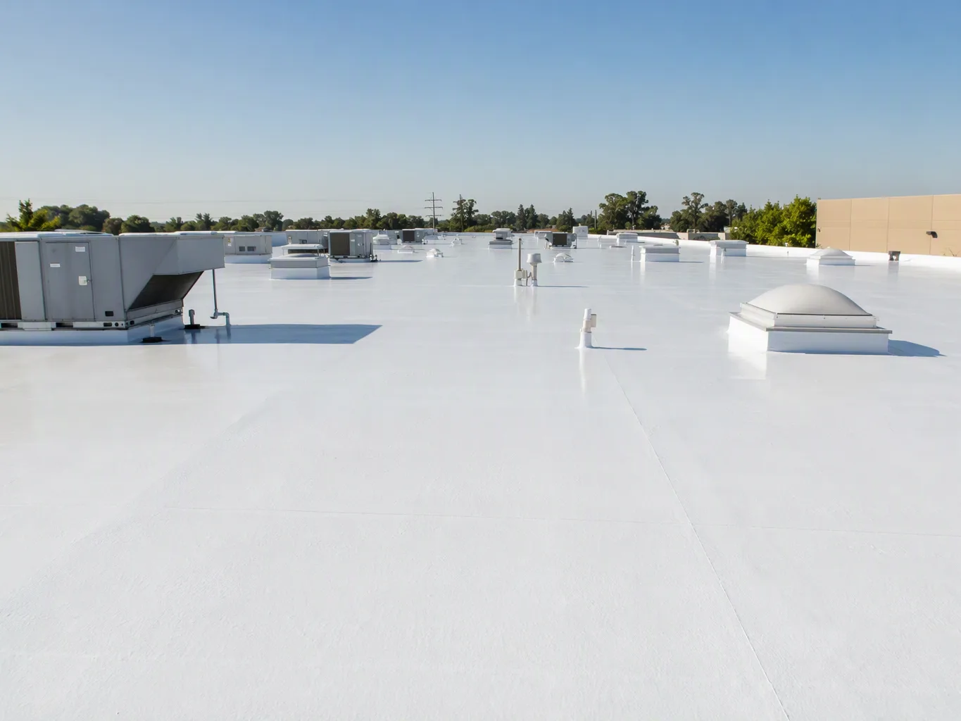 A roofer working on a residential commercial roof coatings job — mid-task, hands, tools and the work itself in sharp focus, the rest of the space softly out of focus